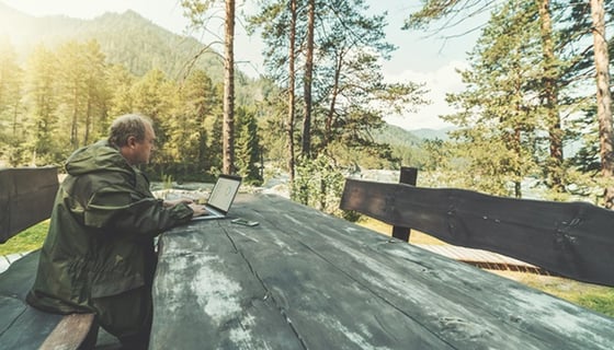 Jäger sitzt im Wald an einem Tisch und ruft ein Dashboard auf einem Laptop auf