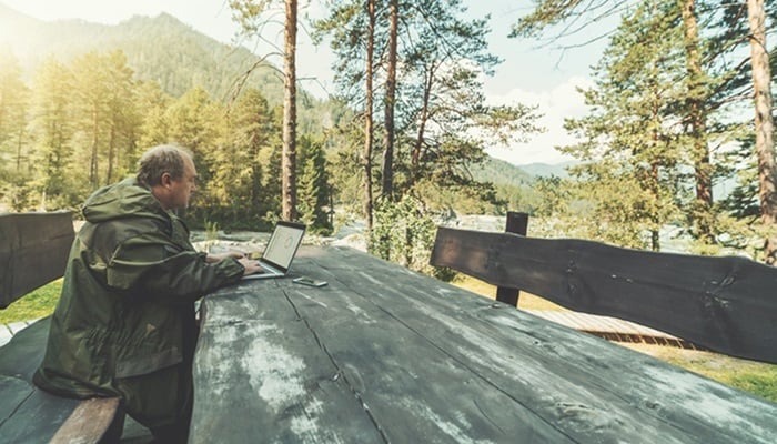 Jäger sitzt im Wald an einem Tisch und ruft ein Dashboard auf einem Laptop auf