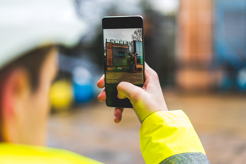 Mann mit Warnjacke macht mit einem Smartphone eine Bild von einem Gebäude