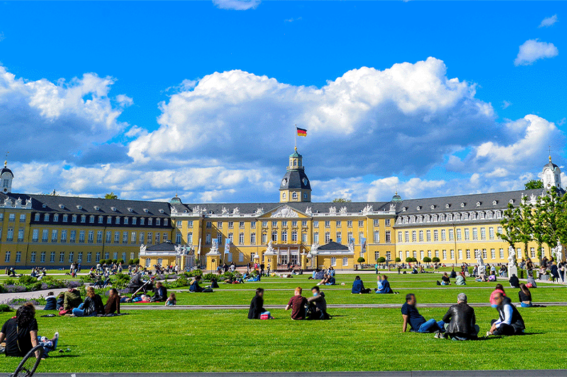 Menschen sitzen auf dem Rasen vor einem Schloß in der Stadt Karlsruhe