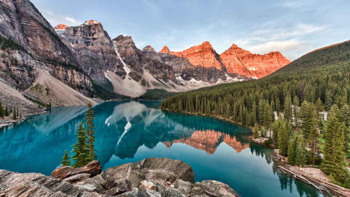 Türkisfarbener Bergsee mit Spiegelung von schroffen Felsbergen und dichtem Nadelwald.