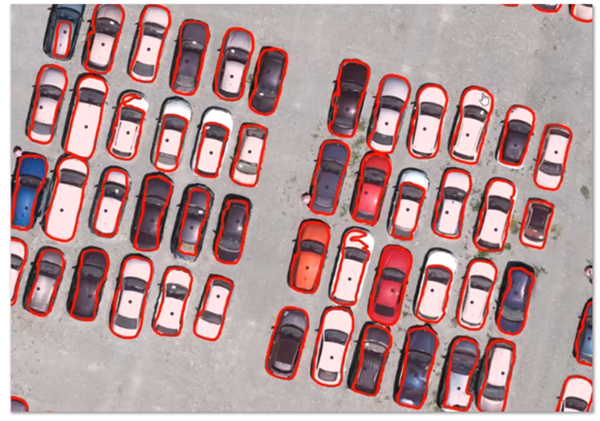 Luftaufnahme eines Parkplatzes mit zahlreichen Autos, die durch rote Umrisse automatisch als Objekte für das Labeling erkannt und segmentiert wurden.