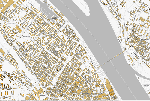 Detaillierte Gebäudekarte eines Stadtgebiets mit hervorgehobenen Gebäudegrundrissen entlang eines Flusses und einer Brückenverbindung.