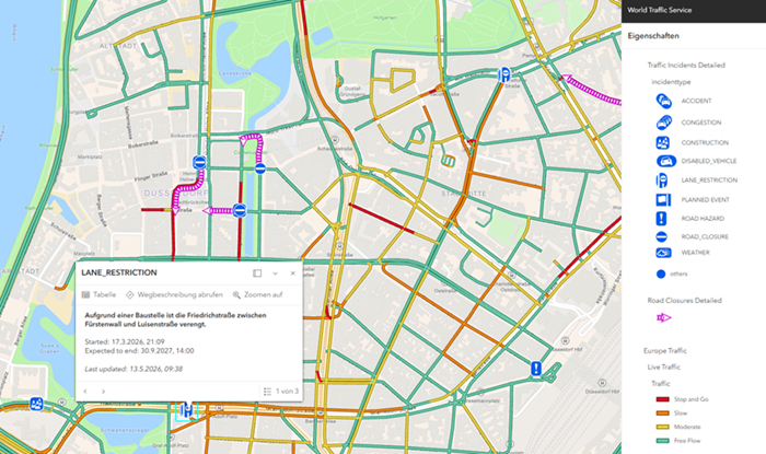 Detailreiche Stadtkarte mit Live-Verkehrsdaten. Straßen sind farblich markiert (grün für fließenden Verkehr, gelb/orange für mäßigen Verkehr und rot für Staus). Mehrere Symbole zeigen Verkehrsereignisse wie Unfälle, Baustellen, Fahrbahnverengungen und Straßensperrungen. Links unten ist ein Hinweisfenster mit der Beschriftung „Lane Restriction“, das Informationen zu einer Baustelle mit Zeitangaben enthält. Rechts befindet sich eine Legende mit verschiedenen Verkehrskategorien und Symbolen.