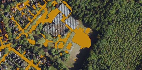 Luftbild einer Industriefläche mit markierten versiegelten Bereichen in Orange, angrenzendem Waldgebiet und Gebäudestrukturen.