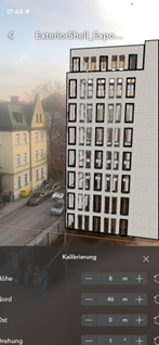 Smartphone-Ansicht einer Augmented-Reality-Anwendung mit platzierter 3D‑Gebäudedarstellung vor einer realen Straßenszene; unten sichtbares Kalibrierungsmenü zur Anpassung von Höhe, Abstand und Ausrichtung.